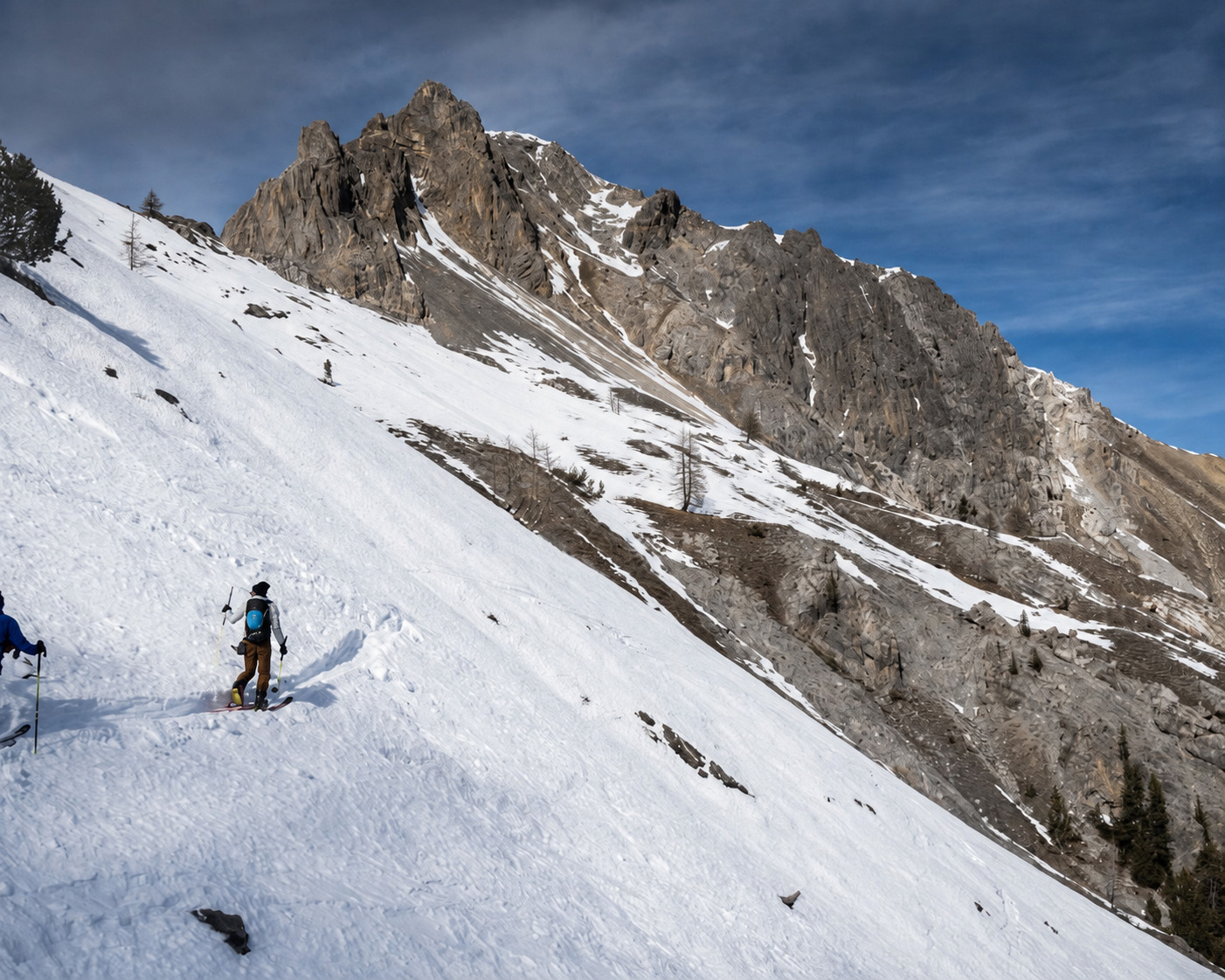 Skieur de randonnée sur une pente face aux crêtes rocheuses du Queyras